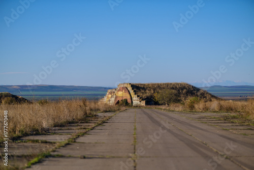 Earth-Covered Bunker With Rusted Door In Open Field Under Clear Blue Sky. Shiraki military airfield base in Republic of Georgia.