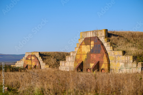 Earth-Covered Bunker With Rusted Door In Open Field Under Clear Blue Sky. Shiraki military airfield base in Republic of Georgia.