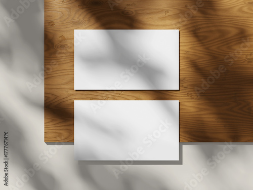 Top view of two business cards on a wooden table with soft lighting and shadows.