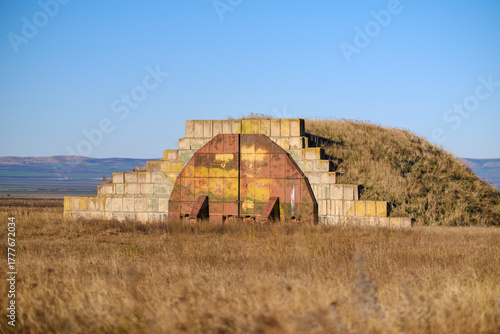 Earth-Covered Bunker With Rusted Door In Open Field Under Clear Blue Sky. Shiraki military airfield base in Republic of Georgia.