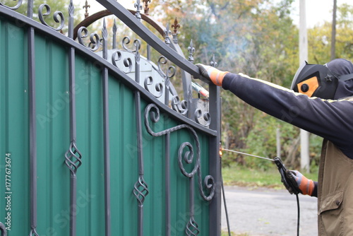 A man repairs a gate at home using a welding machine.
