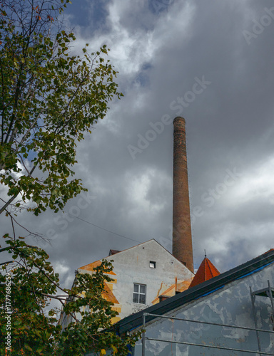 Wallpaper Mural Towering chimney over Skadarska Street in Belgrade, Serbia, where weathered walls and red rooftops meet a moody sky, as sunlight gently breaks through dark clouds and trees Torontodigital.ca