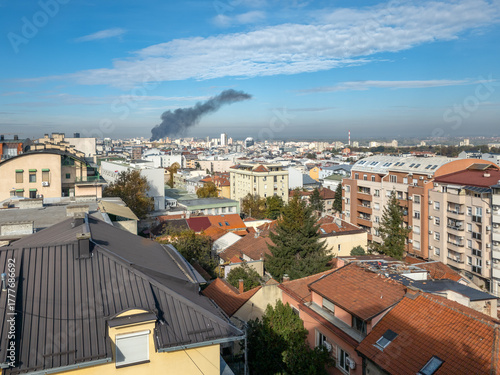 Wallpaper Mural Panoramic view of Belgrade, Serbia, where warm-toned rooftops and modern buildings stretch beneath a vivid blue sky, while a thick plume of black smoke rises in the distance Torontodigital.ca
