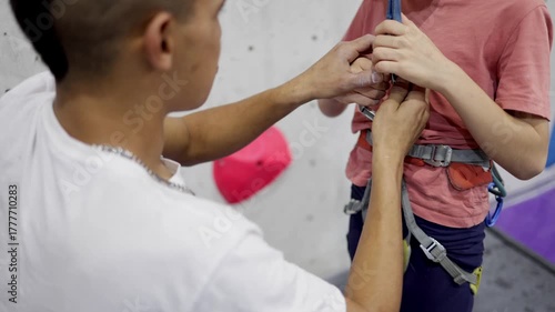Instructor assisting young boy with safety harness for indoor rock climbing, teaching safety methods and belaying techniques at a climbing gym, fostering learning and training