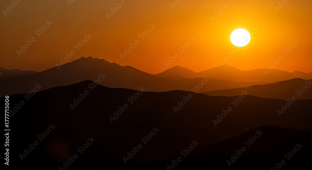 Obraz premium Vibrant sunset over silhouetted mountain ranges casting a warm orange glow across the sky