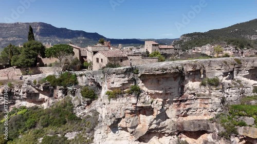 Joven sentada al borde del acantilado de Siurana, en Tarragona, Cataluña. El movimiento del dron revela una impresionante panorámica del pueblo y el paisaje montañoso. libertad, naturaleza, viajes.
