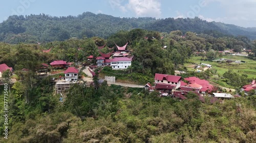 Aerial view of traditional Tongkonan houses with curved roofs on a hillside in Tana Toraja, Indonesia, surrounded by mountains and clouds.	
