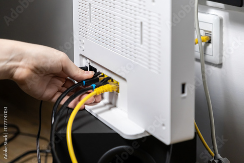 Person's hand skillfully plugs yellow Ethernet and black power cables into a white Wi-Fi router, setting up reliable home internet connection