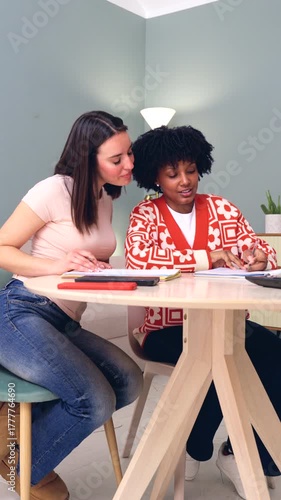 Two multiracial female students studying together at home table with books and tablet, concept of education, learning, teamwork, diversity, friendship, concentration, academic and success.