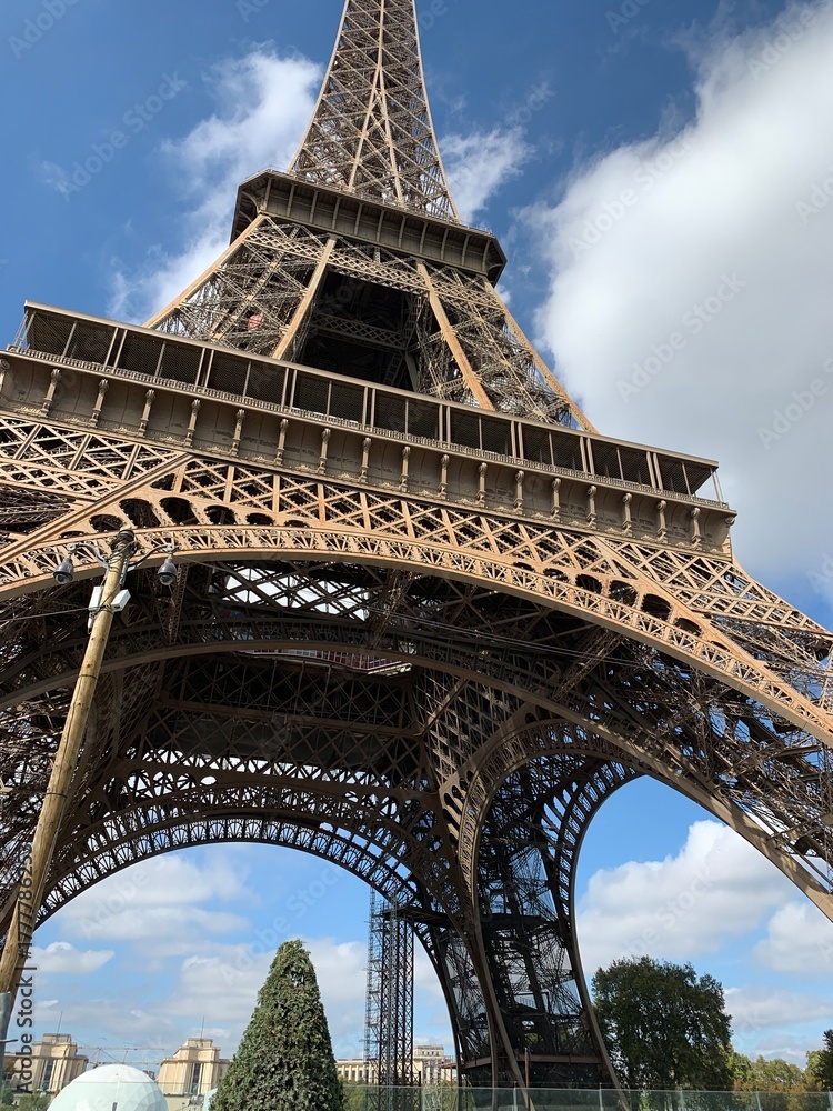 Fototapeta premium Dramatic low-angle photograph looking up through the iron structure of the Eiffel Tower against broken clouds