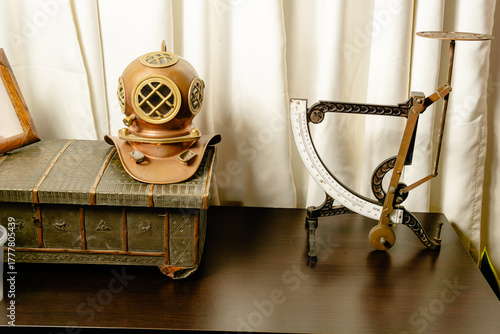 Vintage diving helmet and mechanical steelyard scale displayed against white curtain in Colombian interior.