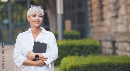 Smiling adult woman posing and holding book. Cheerful pretty adult woman with a book