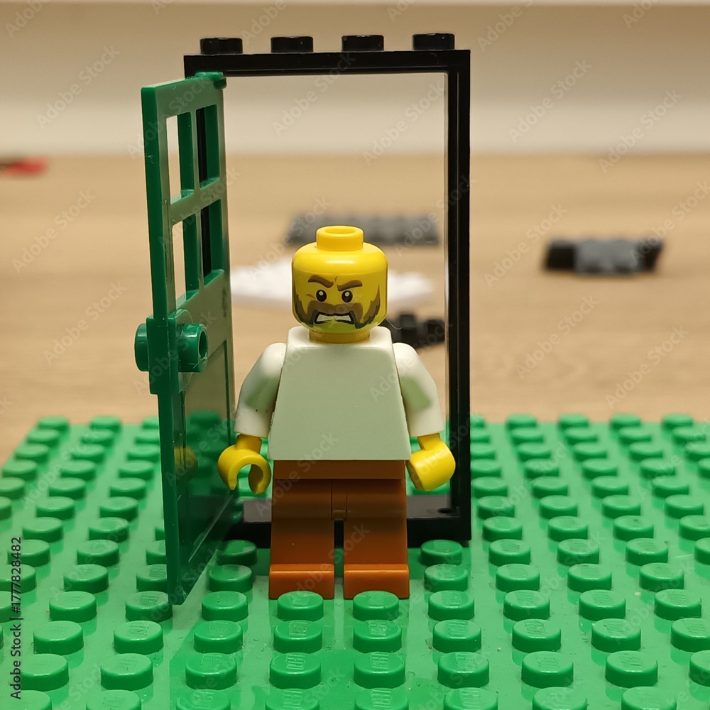 Naklejka premium Lego minifigure with an angry expression stands in an open doorway on a green baseplate, representing a concept of unwelcome entry or disagreement