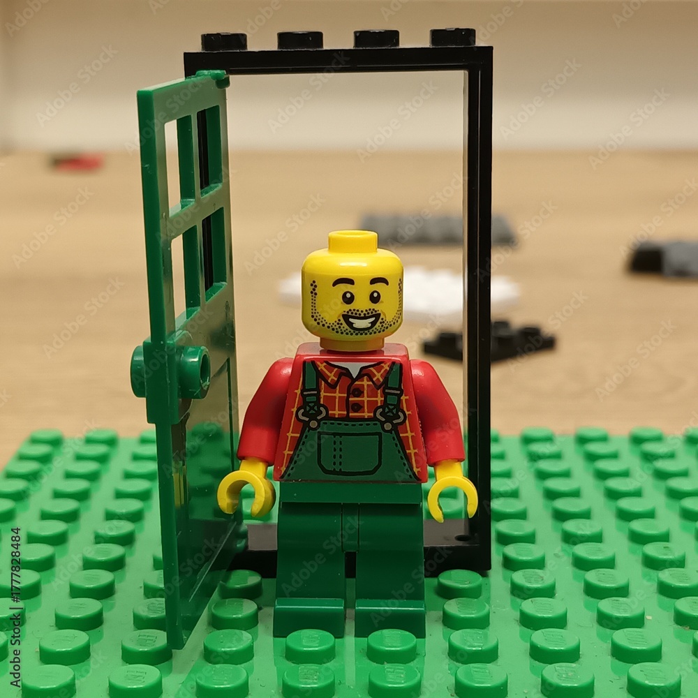 Naklejka premium A Lego farmer minifigure stands smiling cheerfully in a small green doorway on a vibrant green Lego baseplate, depicting a playful scene from the popular construction toy brand