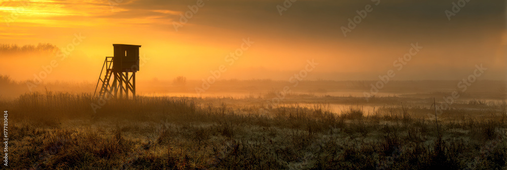 Obraz premium Hunting stand overlooks foggy field at golden dawn in serene landscape