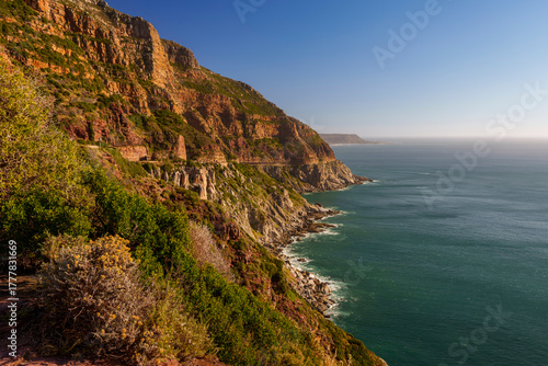 Breathtaking coastline view along Chapman’s Peak Drive near Hout Bay, Cape Town, Western Cape; rugged cliffs, blue ocean, winding road, iconic South African landscape under clear sky.