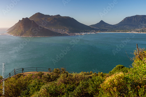 Stunning panoramic view of Hout Bay and coastal mountains from Chapman’s Peak view point, Cape Town, Western Cape, South Africa. A blue bay, rugged peaks, South African scenery beneath a blue sky.