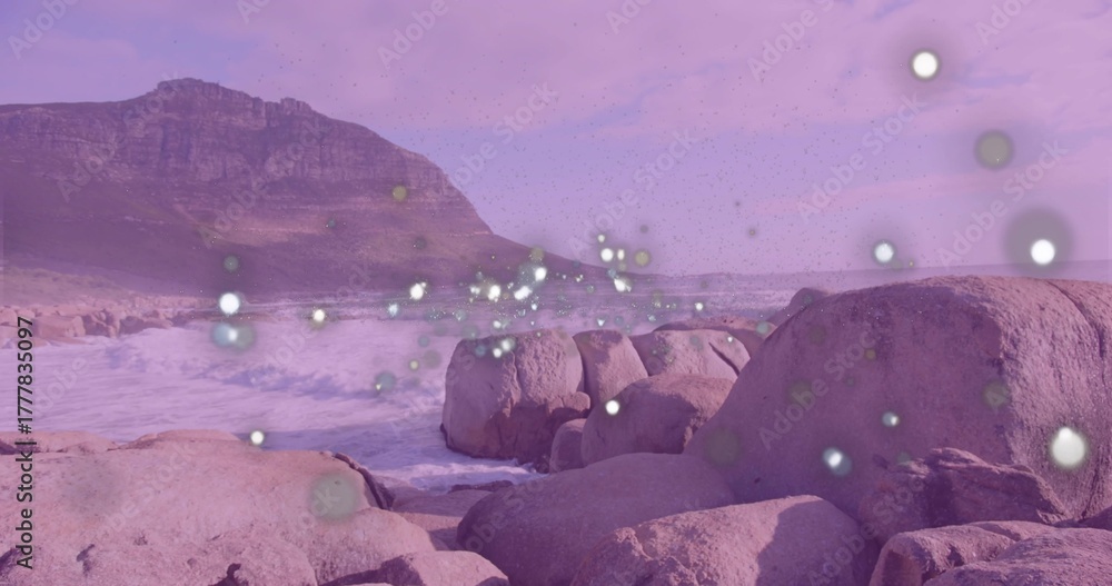 Obraz premium Crashing waves hitting granite boulders on shoreline, rising mountain ridge and floating light orbs