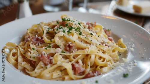 A close up shot of a plate of fettuccine carbonara topped with cheese and parsley on white dish