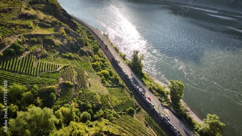 Aerial view of train and cars following river road below steep terraced vineyards. Regional train and river road along vineyards in the Upper Middle Rhine Valley, Rhineland Palatinate, Germany. 