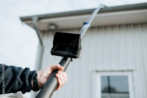 Technician using pole inspection camera to check rain gutter on residential building