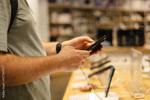 Closeup of man testing smartphone at electronics store showcase.