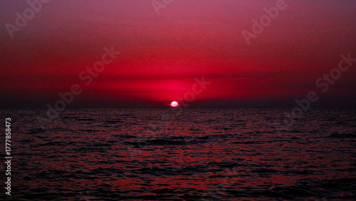 Dramatic red sunset over calm ocean horizon with dark rippling sea water and vibrant twilight sky background for nature, travel, and seascape design