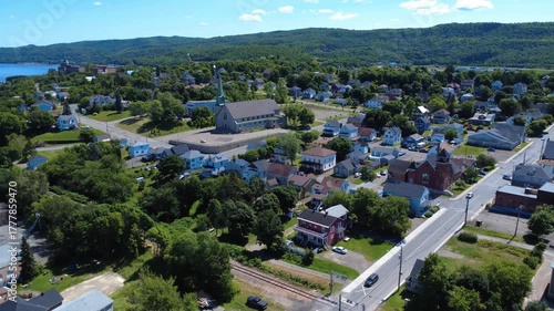 Aerial view of the Notre-Dame-des-Neiges Christian community church and surrounding homes with green hills in the background. Campbellton, New Brunswick, Canada, 2025.