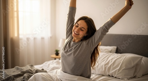 Happy young woman waking up in bed and stretching in the morning. Smiling female feeling refreshed in a sunlit bedroom. Positive start to a new day concept