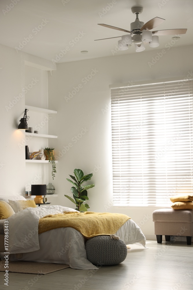 Fototapeta premium Large bed with linens, poufs and shelving unit near window in bedroom