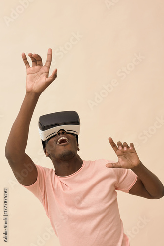 Young Black man wearing virtual reality headset interacting with immersive digital environment, raising arms and gesturing while experiencing simulated technology