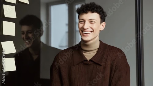 A man in a brown sweater stands in front of a mirror. He is wearing a brown shirt and a brown scarf
