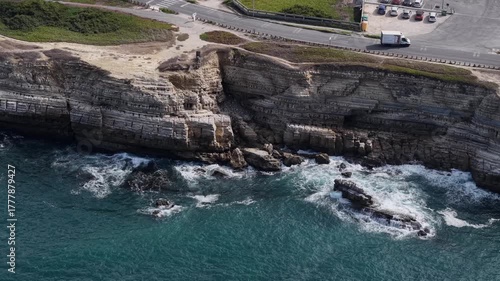 rocky headland extending into blue sea, visible road and dramatic coastal scenery.