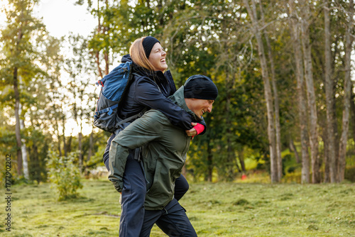 Wallpaper Mural A joyful woman rides piggyback on a smiling man during a playful hiking moment in a forest clearing, both dressed in outdoor gear and surrounded by trees Torontodigital.ca