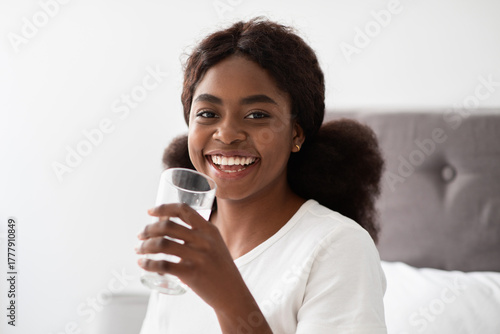 Wall Mural Healthy african american young lady with bushy hair smiles while drinking fresh water after waking up