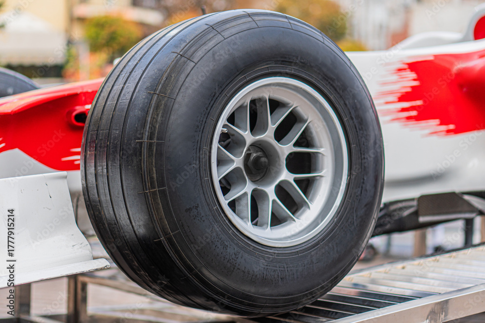 Obraz premium Formula 1 car with front right wheel missing, showing wheel hub and suspension components Red vehicle with white accents and UPS sponsorship branding Setting suggests a maintenance area or pit stop