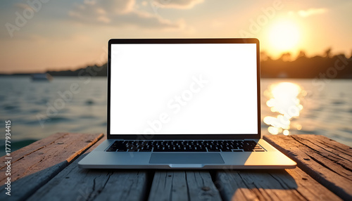 Laptop with blank screen on a wooden dock at sunset over the water
