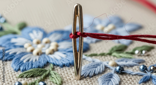 Embroidery close-up features a needle with red thread on textured fabric with floral design. Ideal for craft projects, textile art, or fashion content.