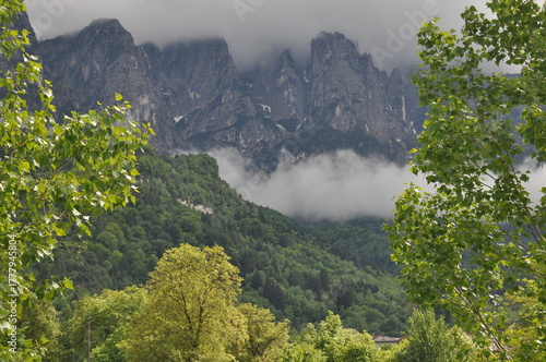 Majestic mountains rise above lush green trees under cloudy skies in a tranquil landscape