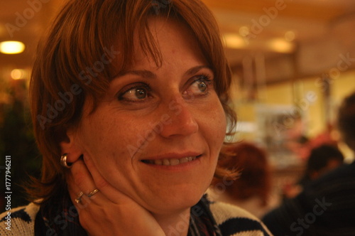 Woman smiling warmly in a cozy restaurant during an evening gathering with friends, showcasing a joyful moment of connection and warmth