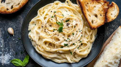 Delicious spaghetti alfredo with creamy sauce and toasted bread on a dark plate, garnished with basil