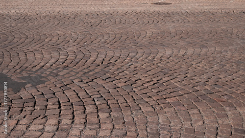 Old market square pavement made of natural stone blocks arranged in curved patterns. 