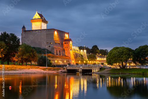 Narva Castle illuminated at night by the river, Estonia.