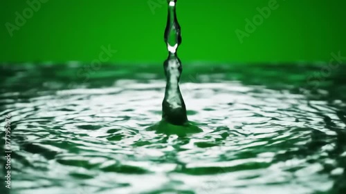 Closeup of a single water droplet falling and creating a perfect splash and ripple effect on a calm water surface with a vibrant green background symbolizing purity freshness and environmental concep.