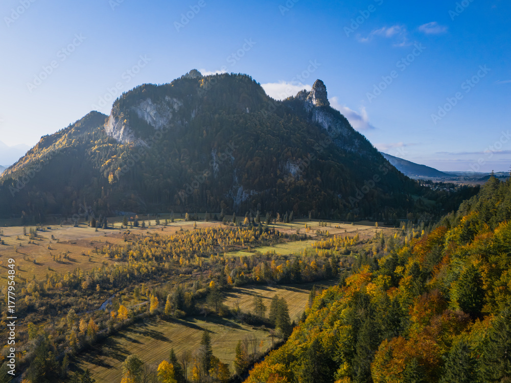 Obraz premium Ettaler Weidmoos autumn aerial with the Ammer River, Kofel and Rappenkopf under clear blue sky; warm valley tones, tranquil mood, ideal for travel ads.