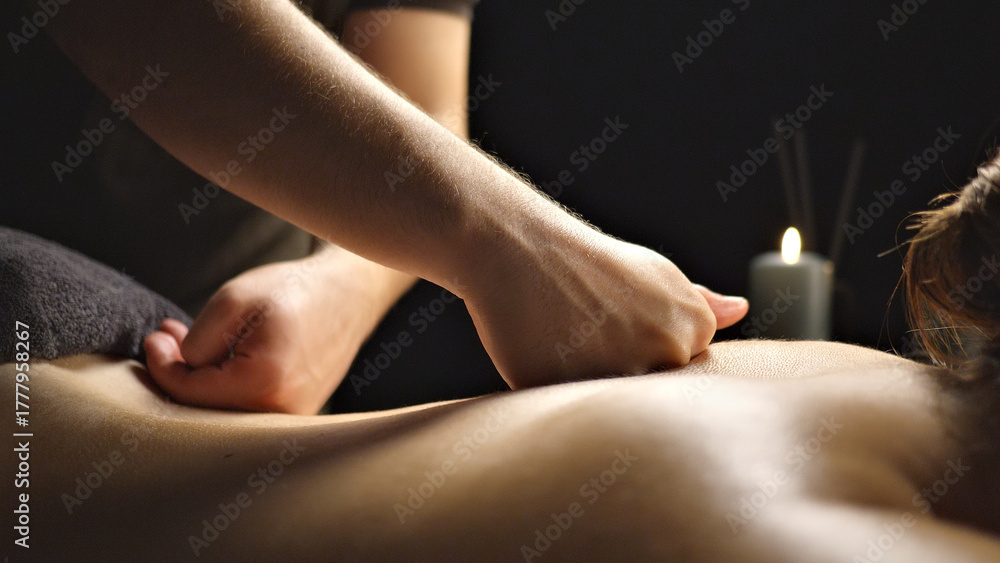 Obraz premium A close-up of a massage therapist's hands kneading a client's back, promoting relaxation and relief. The serene setting with a lit candle enhances the calming atmosphere.