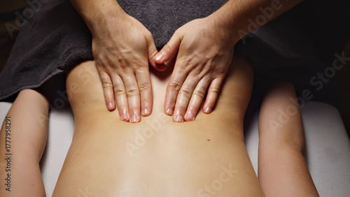A massage therapist's hands gently press on a client's lower back, providing a soothing massage in a serene spa setting. The focus is on alleviating tension and promoting well-being.