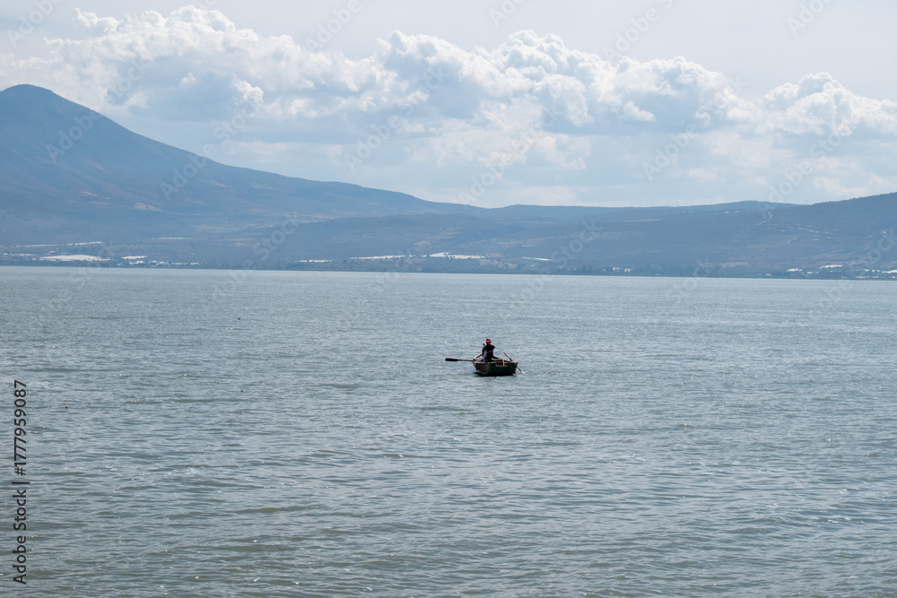 Obraz premium Solitary fisherman on wooden boat in the middle of Lake Chapala with distant mountains in view