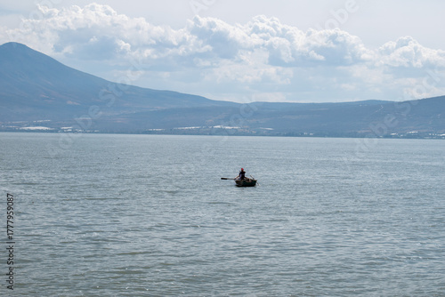 Solitary fisherman on wooden boat in the middle of Lake Chapala with distant mountains in view