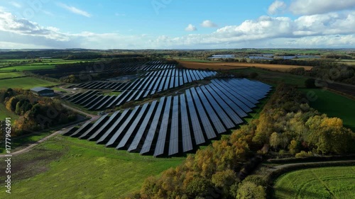 Drone flyover of utility solar field with maintenance tracks and inverter stations in a green landscape near Nottingham
